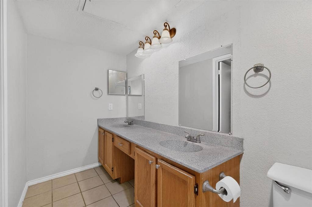 5750 Phoenix Drive, #6, Dallas, TX 75231 Dual sink vanity with wood-finish cabinetry, speckled countertop, and tiled flooring