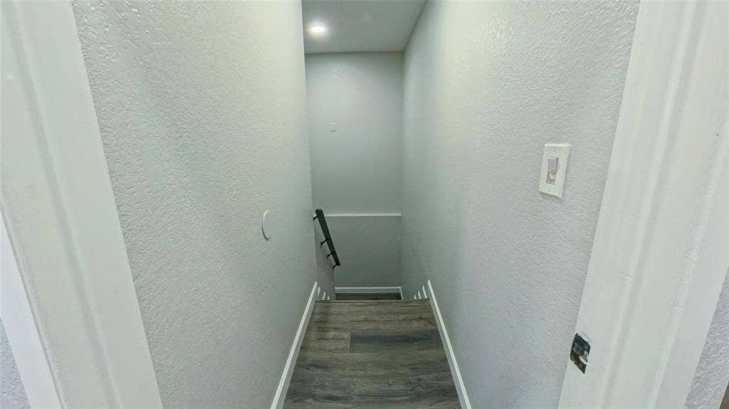 Staircase featuring wood-finish flooring, neutral wall paint, recessed lighting, and a metal handrail
