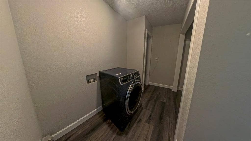 Utility area featuring wood-finish flooring, textured walls, and a recessed plumbing connection