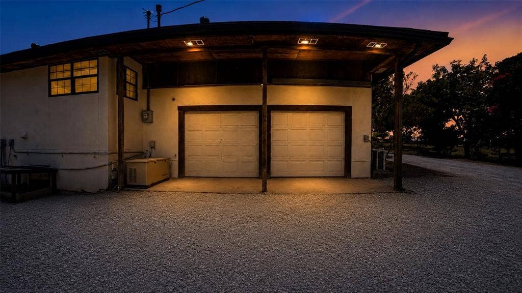 Attached two-car garage featuring dual overhead doors, a covered exterior canopy, and gravel driveway