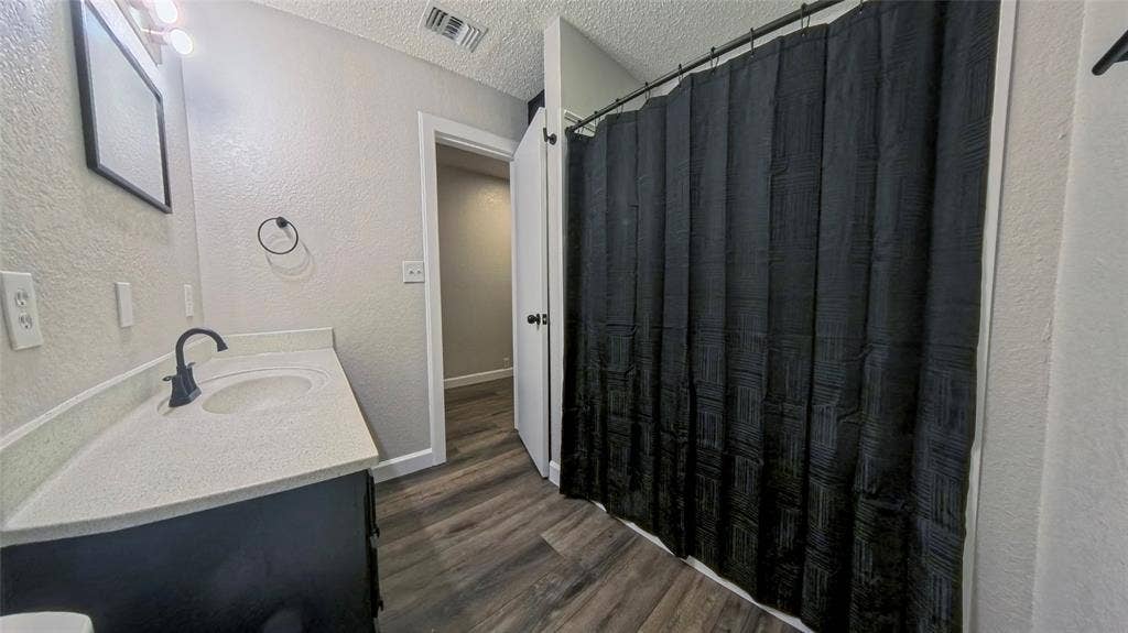 Bathroom featuring a stone-composite countertop with an integrated basin, matte black faucet, dark-finish cabinetry, and wood-finish flooring