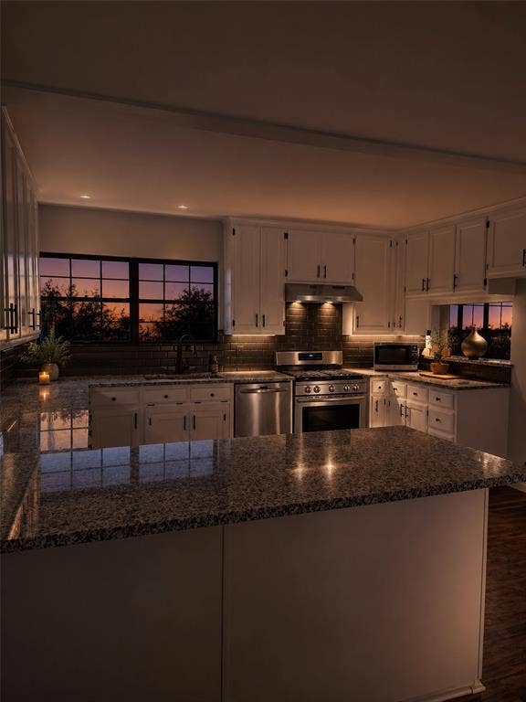 Kitchen featuring white cabinetry, stone countertops, dark-toned tile backsplash, and stainless steel appliances