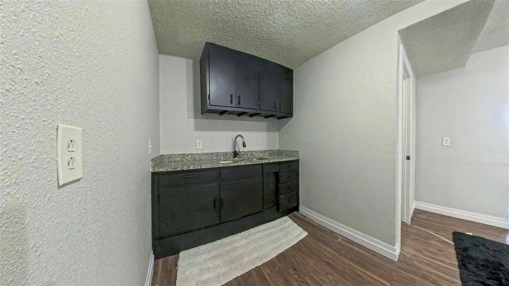 Dark cabinetry featuring built-in storage, stone-finish countertop, undermount sink with goose-neck faucet, and wood-finish flooring