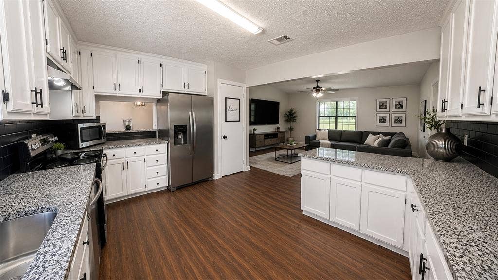 Kitchen featuring white cabinetry with matte black hardware, stone-finish countertops, black tile backsplash, stainless steel appliances, and wood-finish flooring