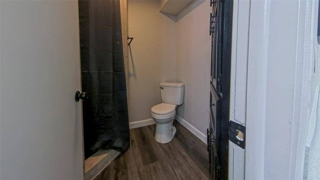 Bathroom featuring wood-finish flooring, a two-piece toilet, and a built-in cabinet with matte black hardware