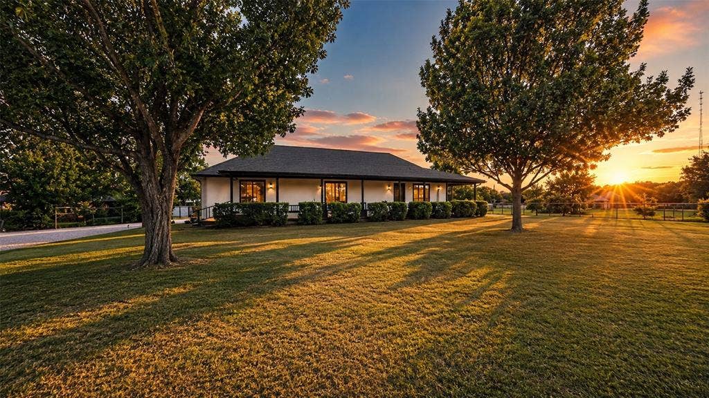Exterior featuring a covered wrap-around porch, stucco siding, a hip roof, and expansive lawn with mature trees