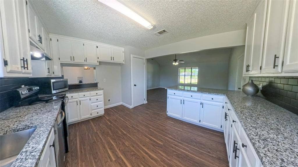 Kitchen featuring white shaker-style cabinetry, speckled stone countertops, dark subway tile backsplash, stainless steel appliances, and wood-finish flooring