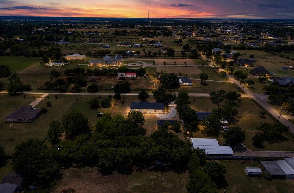 Aerial perspective featuring expansive acreage, mature tree clusters, and a paved circular driveway
