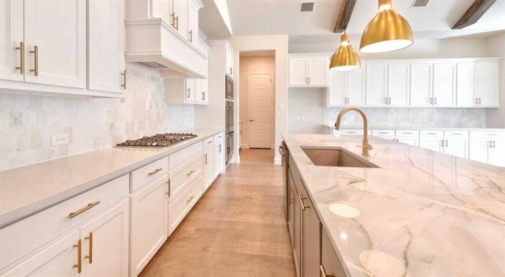 Kitchen featuring white shaker cabinetry, quartz countertops, a stone tile backsplash, a large central island with a gooseneck faucet, and exposed ceiling beams
