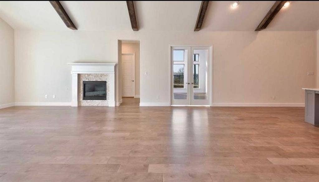 Vaulted ceiling featuring exposed wood beams, wood-finish flooring, fireplace with stone surround and mantle, and French doors