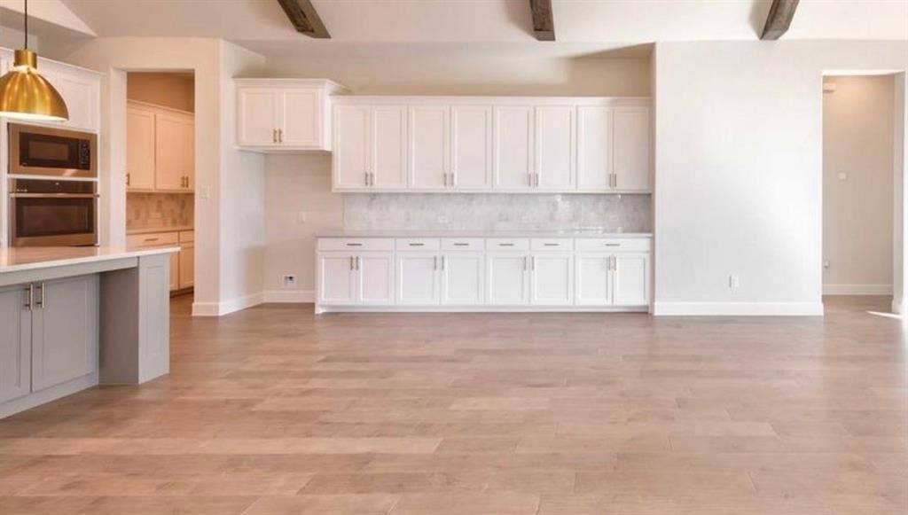 Kitchen featuring white cabinetry, wood-finish flooring, stone-material backsplash, ceiling-mounted beams, and built-in stainless steel double ovens