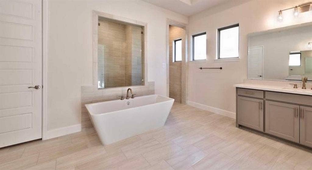 Freestanding soaking tub, walk-in tile surround shower, dual-sink vanity with neutral cabinetry, large-format tile flooring, and oversized wall-mounted mirror