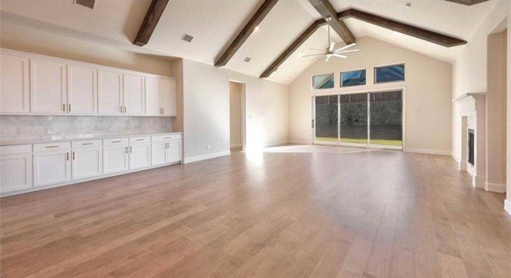 Vaulted ceiling with exposed wood beams, wood-finish flooring, extensive built-in white cabinetry, full-height sliding glass doors with transom windows, and a built-in fireplace