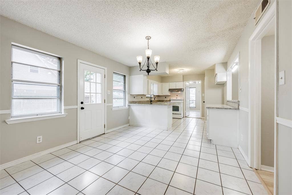 Kitchen featuring a peninsula with stone-finish countertops, white cabinetry, tile flooring, and a multi-light chandelier