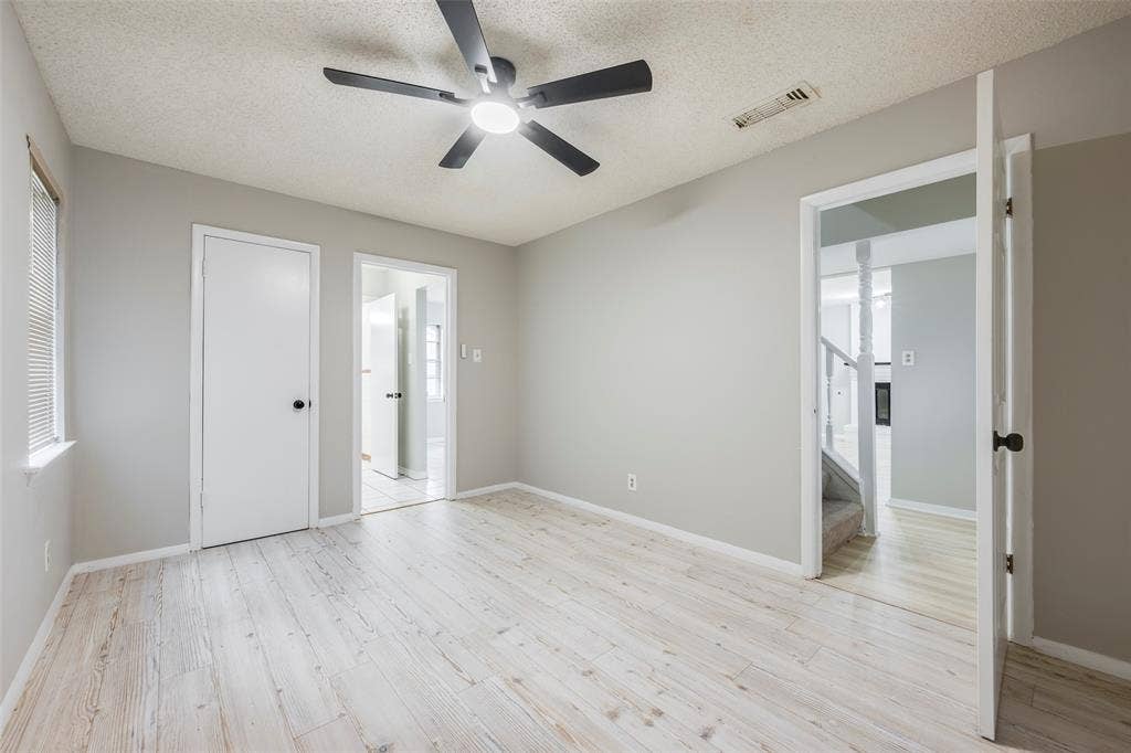 Room featuring wood-finish flooring, a matte black ceiling fan with integrated lighting, neutral wall paint, and multiple interior doors