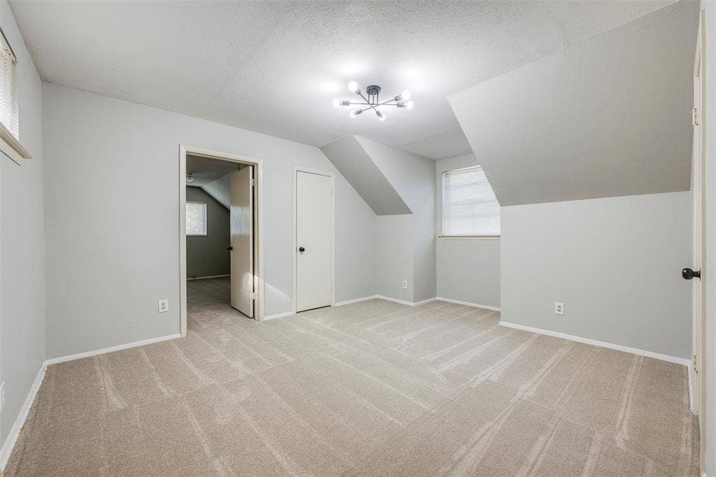 Neutral-toned carpeted flooring, multi-arm flush-mount ceiling lighting, sloped ceiling architecture, and interior doors with spherical hardware