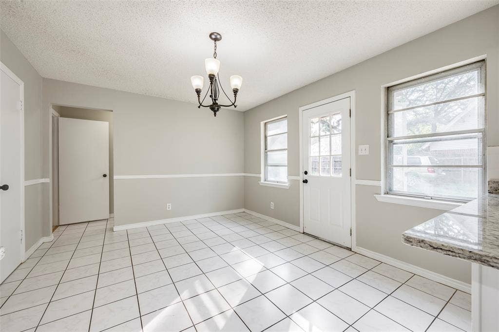 Neutral-toned room featuring tile flooring, chair rail molding, a multi-light chandelier, and a exterior door with a glass pane