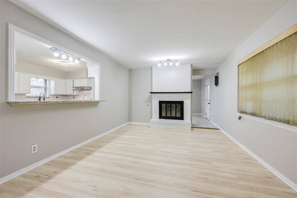 Living area featuring light wood-finish flooring, a white brick fireplace with a dark mantel, a pass-through opening, stone-finish countertops, and flush-mount lighting