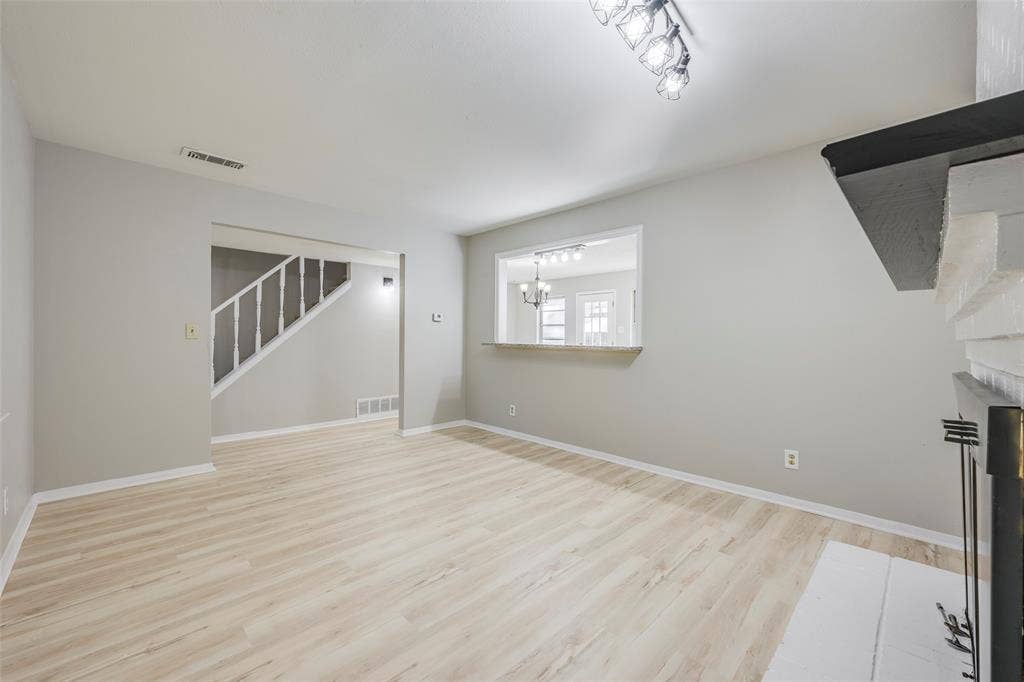 Living area featuring wood-finish flooring, a painted brick fireplace surround with a black mantel, a pass-through opening, and a staircase with a white railing