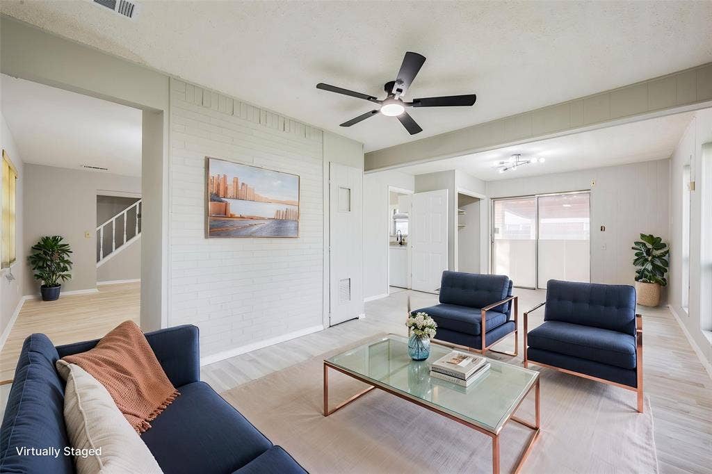 Living area featuring painted brick accent wall, wood-finish flooring, and a ceiling fan with integrated lighting