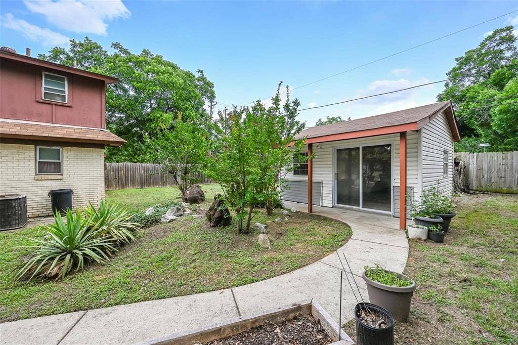 Backyard featuring a detached structure with sliding glass doors, a concrete pathway, mature landscaping, and wood privacy fencing