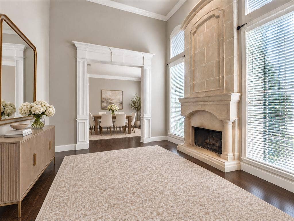 High ceilings featuring crown molding, floor-to-ceiling stone fireplace, wood-finish flooring, and classical millwork framing the doorway