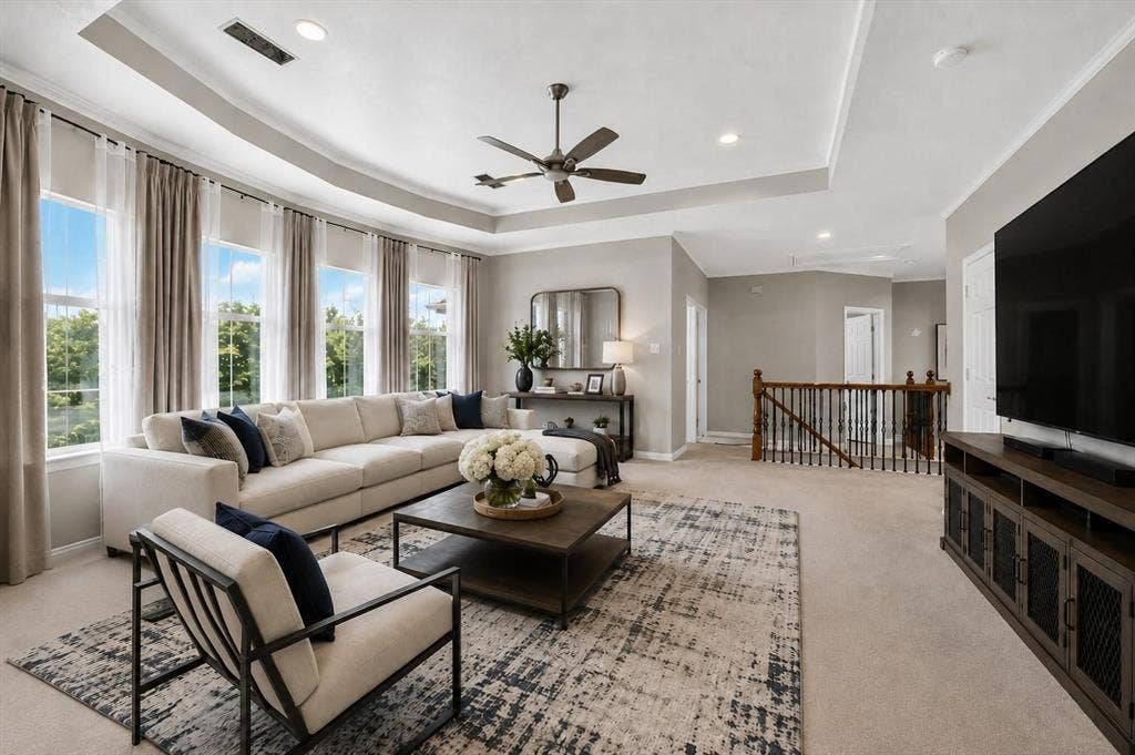 Tray ceiling featuring a central multi-blade ceiling fan, expansive windows, recessed lighting, and a staircase with stained wood handrails and iron balusters