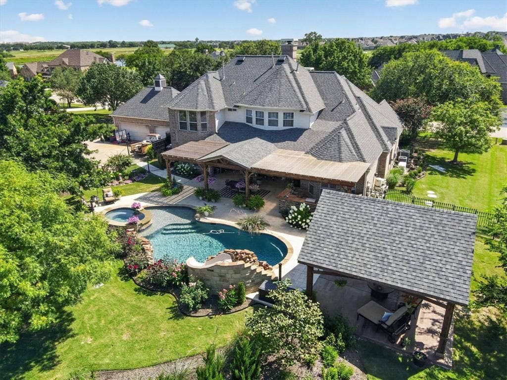 Rear exterior featuring a multi-level stone pool with integrated spa and rock water feature, expansive covered patio with built-in kitchen, detached timber-frame pavilion, and mature landscaping