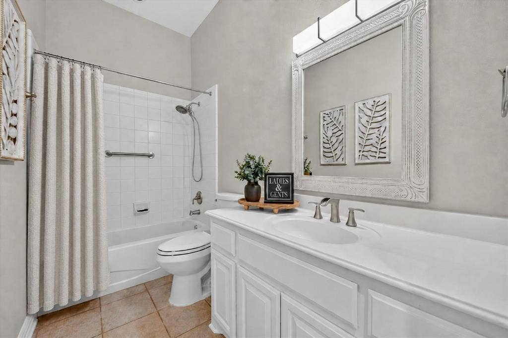 Bathroom featuring a white vanity cabinet with an integrated countertop, wall-mounted light fixture, decorative framed mirror, and a tub-shower combination with ceramic tile surround