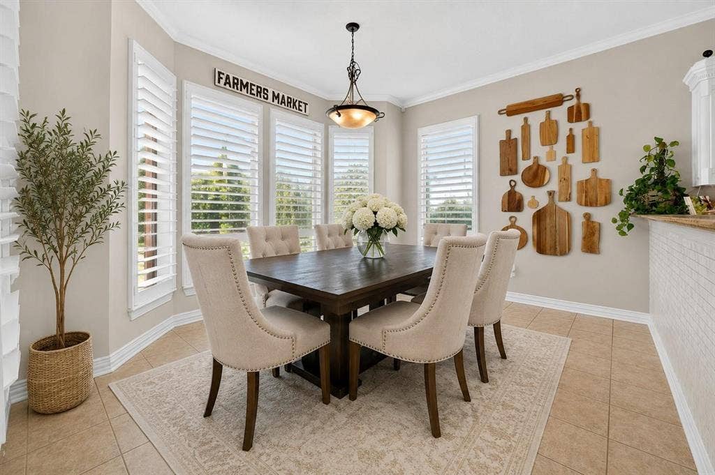 Dining area featuring a bay window, plantation shutters, neutral tile flooring, crown molding, and a tiered pendant light fixture
