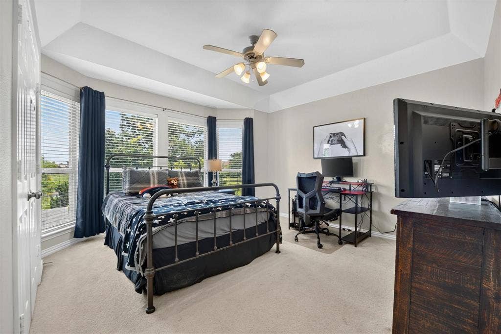 Tray ceiling featuring a central light fixture with an integrated ceiling fan, neutral carpeting, and multi-paneled windows