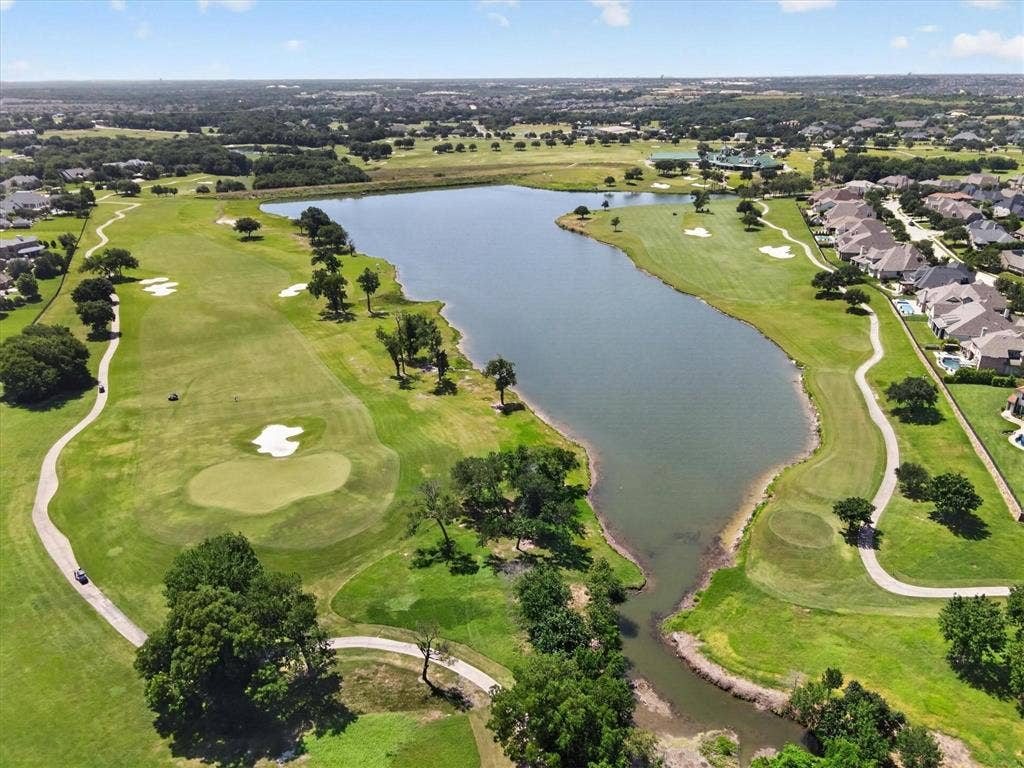 Aerial perspective of a golf course featuring manicured greens, sand bunkers, expansive water features, and paved cart paths