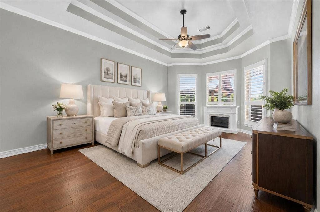 Tray ceiling with crown molding, wood-finish flooring, fireplace with a custom mantel, and windows equipped with plantation shutters