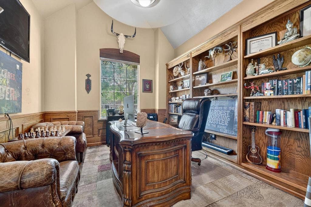 Vaulted ceiling with a centered light fixture, extensive floor-to-ceiling built-in wood shelving, wood wainscoting, and a central window with an arched wood header