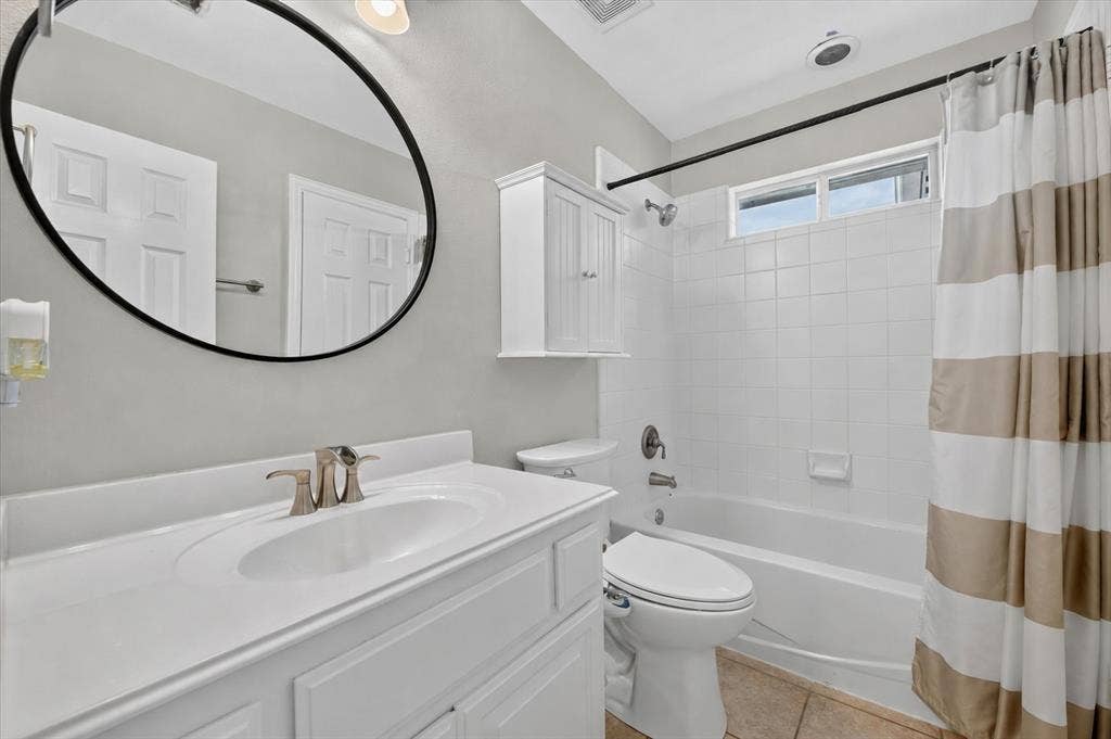Bathroom featuring a vanity with an integrated basin, a large oval mirror, a wall-mounted medicine cabinet, and a tiled shower-tub combination