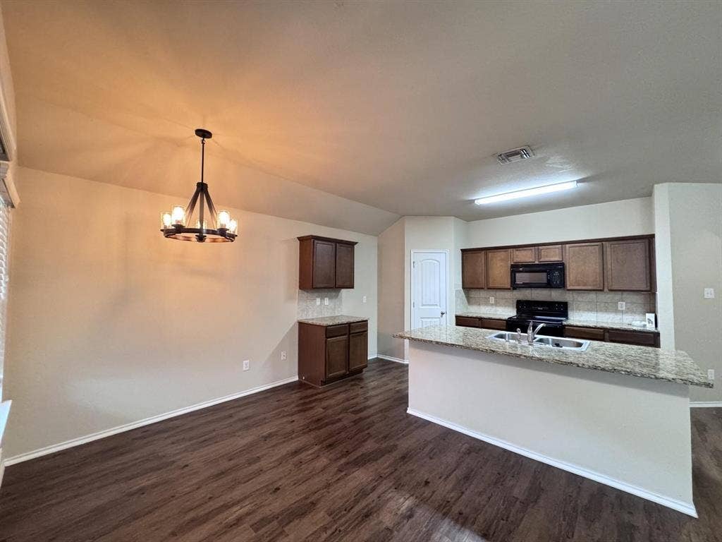 2105 Meadow Park Drive, Princeton, TX 75407 Kitchen featuring dark wood-finish cabinetry, stone-style countertops, wood-finish flooring, a stainless steel double-basin sink, and a multi-arm wagon wheel chandelier