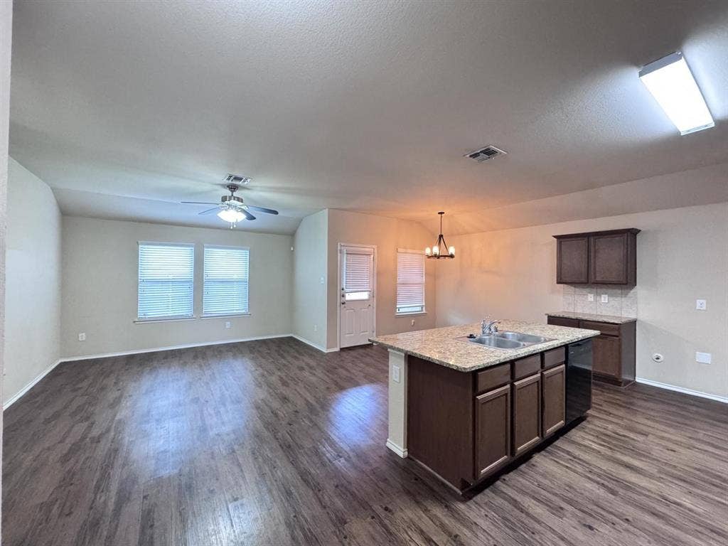 2105 Meadow Park Drive, Princeton, TX 75407 Open-concept interior featuring wood-finish flooring, a kitchen island with stone-finish countertops, dark wood-finish cabinetry, a vaulted ceiling with an integrated ceiling fan, and a multi-light chandelier
