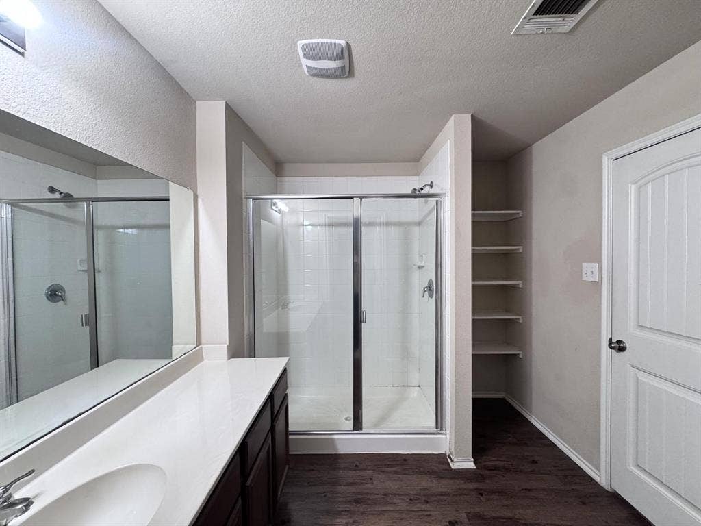 2105 Meadow Park Drive, Princeton, TX 75407 Full-width wall mirror, wood-finish flooring, glass-enclosed shower with tile surround, solid-surface vanity countertop, and built-in wall shelving