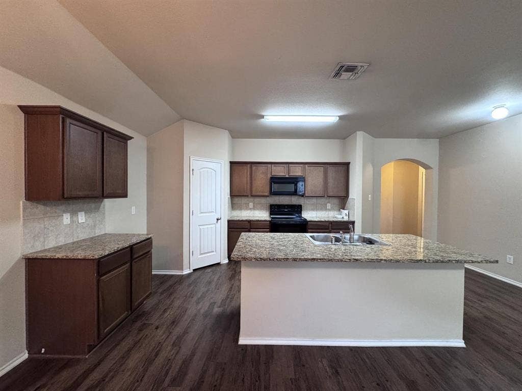 2105 Meadow Park Drive, Princeton, TX 75407 Kitchen featuring dark wood-finish cabinetry, stone-style countertops, a central island with an integrated dual-basin sink, and wood-finish flooring