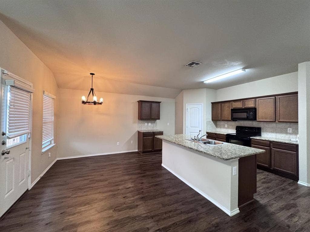 2105 Meadow Park Drive, Princeton, TX 75407 Kitchen featuring an island with a stone-surface countertop, dark-finish cabinetry, wood-finish flooring, and a multi-light chandelier