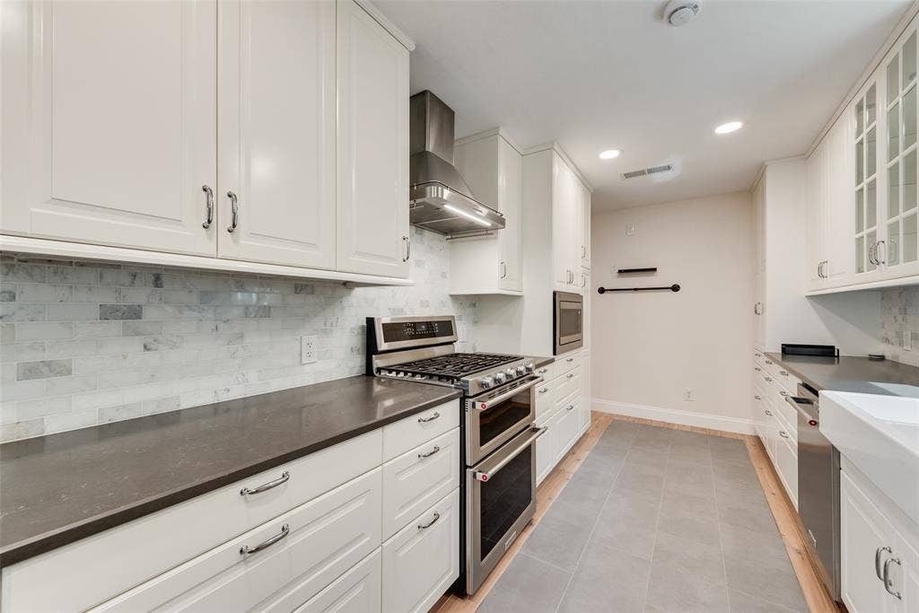 620 Cox Drive, Irving, TX 75062 Kitchen featuring white shaker-style cabinetry, stainless steel double oven with gas cooktop, stone tile backsplash, contrasting dark countertops, and large-format porcelain tile flooring