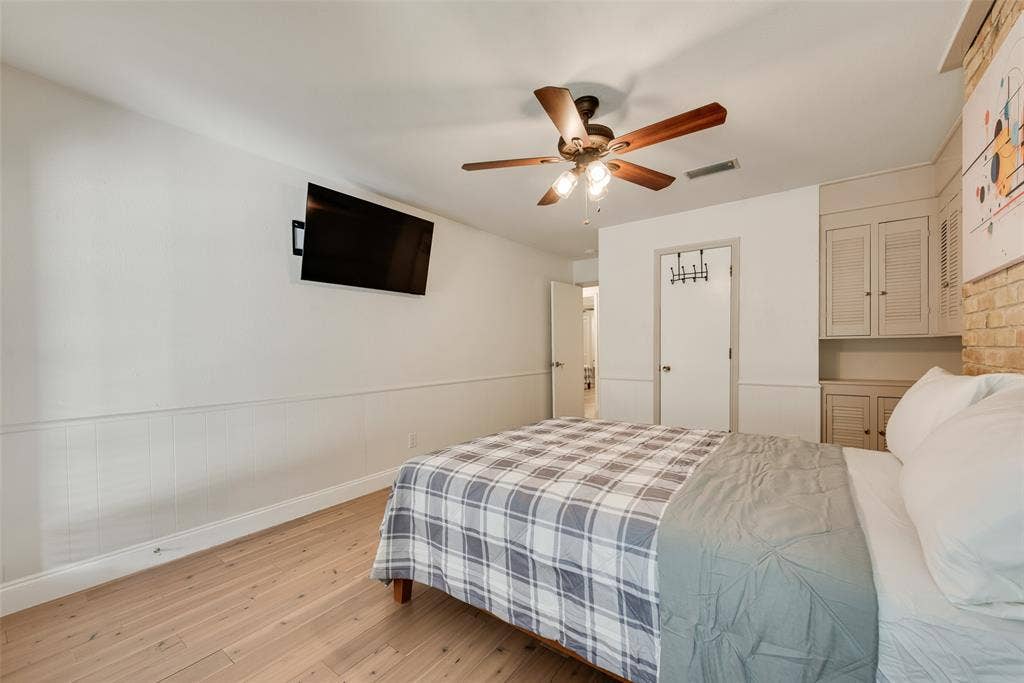 620 Cox Drive, Irving, TX 75062 Wood-finish flooring, ceiling fan with integrated lighting, wall-mounted cabinetry with louvered doors, and brick accent wall