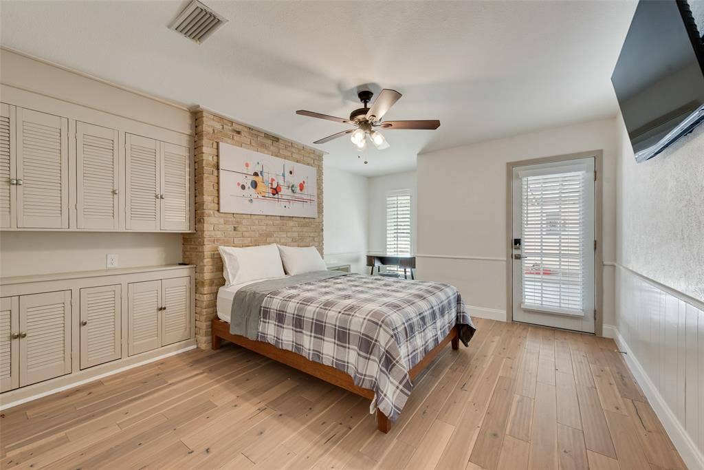 620 Cox Drive, Irving, TX 75062 Interior space featuring wood-finish flooring, exposed light-toned masonry accent wall, built-in louvered cabinetry, beadboard wall paneling, and a ceiling fan with integrated lighting