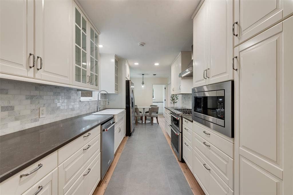 620 Cox Drive, Irving, TX 75062 Kitchen featuring floor-to-ceiling cabinetry, stone-surface countertops, decorative stone-tile backsplash, undermount apron-front sink, and stainless steel built-in appliances