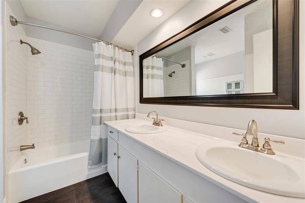 620 Cox Drive, Irving, TX 75062 Dual-sink vanity with white countertop, subway-tiled tub surround, full-width framed mirror, recessed lighting, and dark-toned flooring