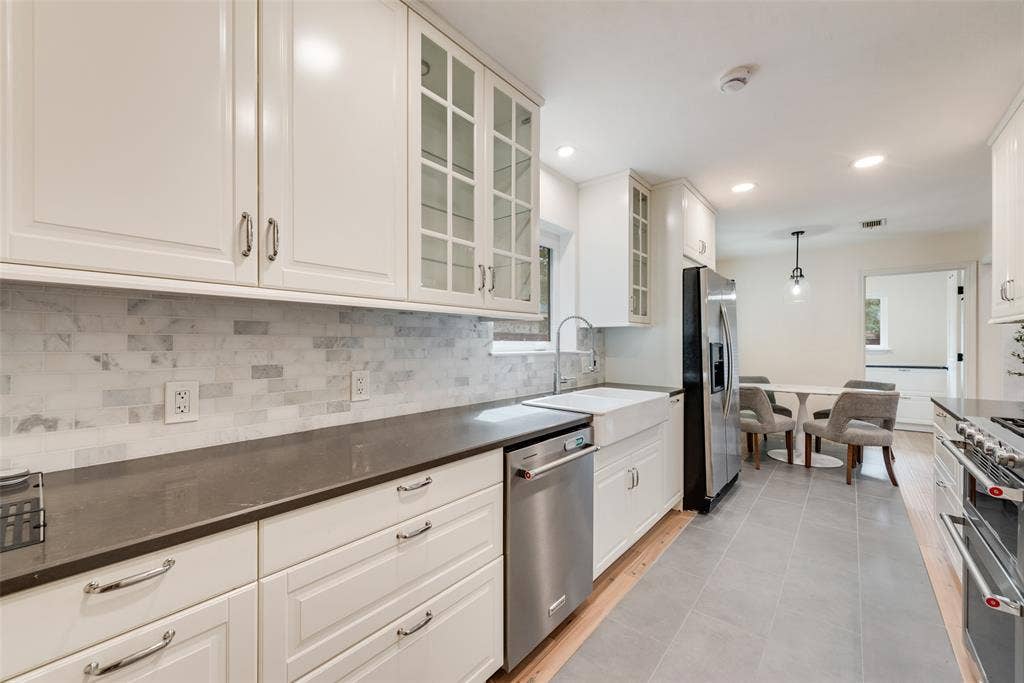 620 Cox Drive, Irving, TX 75062 Kitchen featuring white cabinetry with glass-front uppers, solid-surface countertops, stone-tile backsplash, stainless steel appliances, and a farmhouse-style apron sink