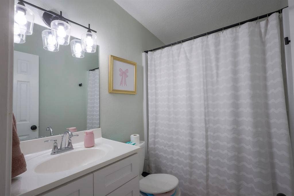 White vanity cabinet with an integrated sink, polished metal faucet, large rectangular mirror, and four-light glass vanity fixture