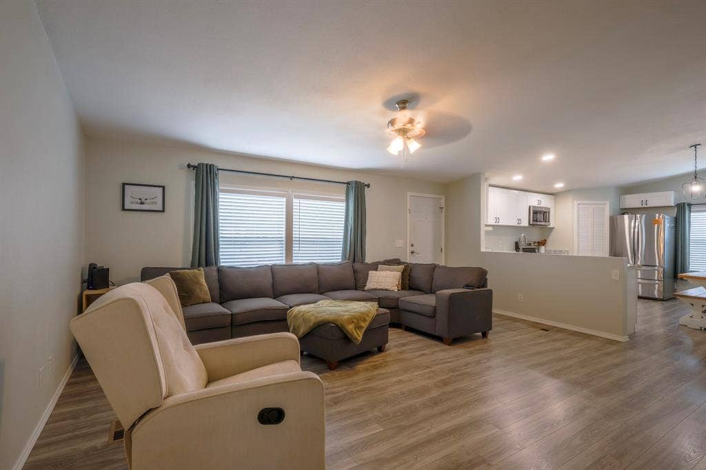 Living area featuring wood-finish flooring, recessed lighting, and a ceiling fan, including a kitchen with white cabinetry and stainless steel appliances