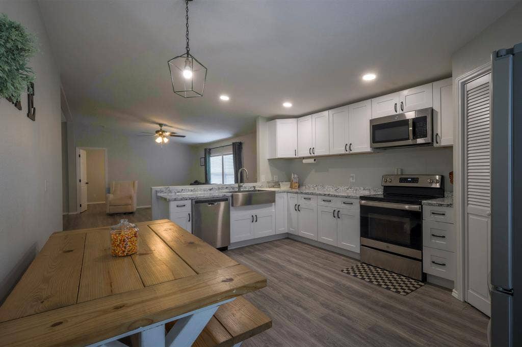 Kitchen featuring white shaker-style cabinetry, stainless steel farmhouse-style sink, stone-finish countertops, stainless steel appliances, and wood-finish flooring