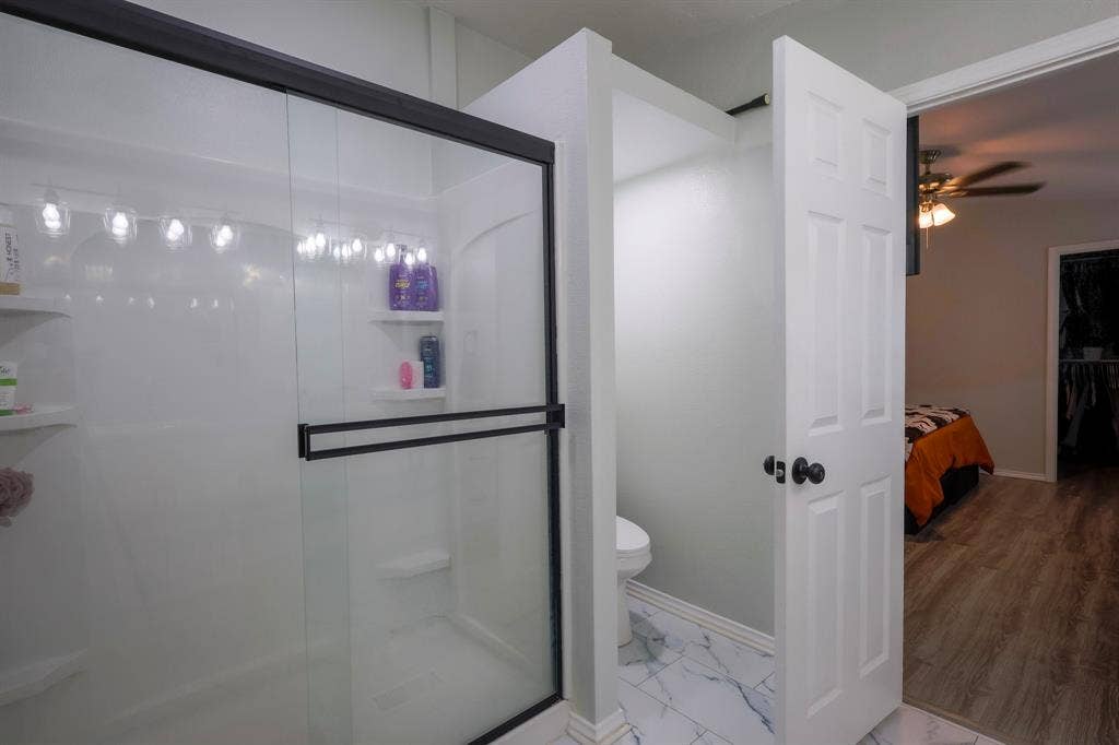 Walk-in shower with matte black sliding glass doors, integrated shelving, and white tile flooring with gray veining